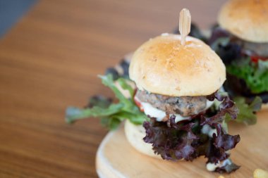 Küçük hamburgerler ızgara domuz eti, salata ve domatesler ahşap tabağa konur.