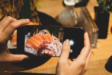 Sashimi Japon yemeklerini akıllı telefonla çeken eller.