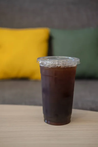 Iced black coffee in a glass on wood table with sofa background