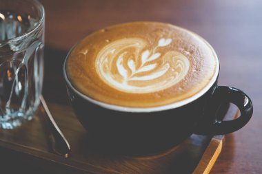 Kahve dükkanındaki ahşap tepside soğuk suyla servis edilen bir fincan sıcak latte sanat kahvesi.