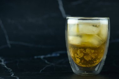 Siyah mermer zemin üzerinde buz olan bir bardak bira.