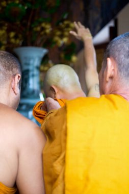 Taylandlı keşiş, Budist adam için portakal rengi keşiş kıyafeti giymeye yardım ediyor. Yeni atanmış Budist keşiş törende dua ediyor..