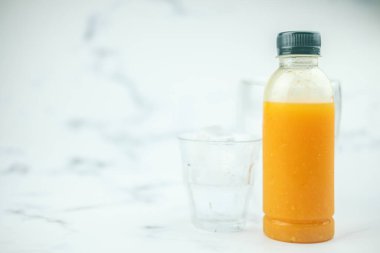 Plastik şişede taze portakal suyu, mermer zemin üzerinde buzla servis edilir.