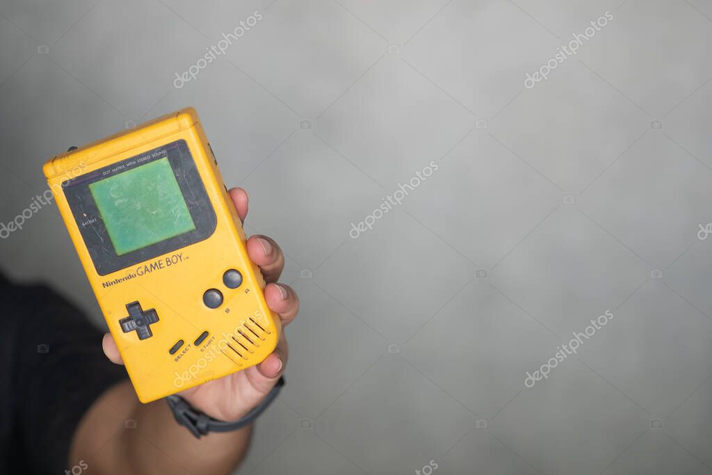 Samut Prakan, Thailand - April 26 2020 : Young man hand holding of an original Nintendo handheld video game device Game boy (1989).