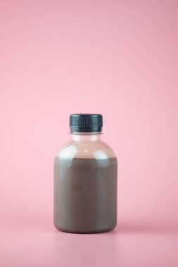 Küçük içecek şişesinde çikolatalı süt ve pembe arka planda siyah başlık.