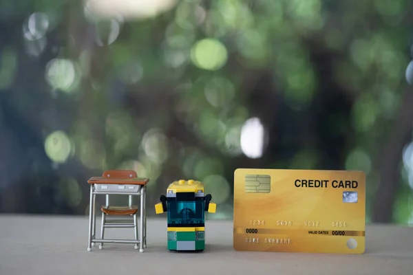 Miniature student table and school bus with credit card on wood table. Concept of pay fees for general education or elementary education