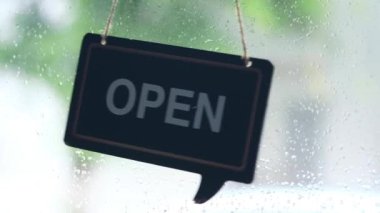 Dükkânın kapısında asılı ahşap siyah bir tabela var.