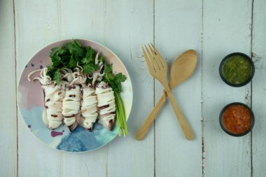 Buharda pişirilmiş kalamar kişniş ile servis edilir ve baharatlı deniz ürünleri sosuyla yenir.