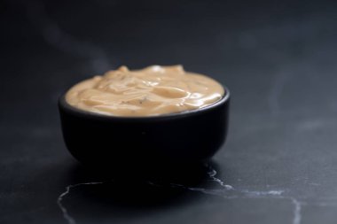 Siyah arka planda siyah bir fincanda Sezar salatası kreması.