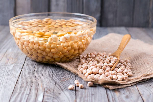 Uncooked chickpeas in wooden spoon on wooden background — Stock Photo, Image