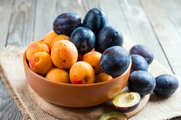 Літні фрукти сливи та абрикоси в мисці на дерев'яному фоні — стокове фото