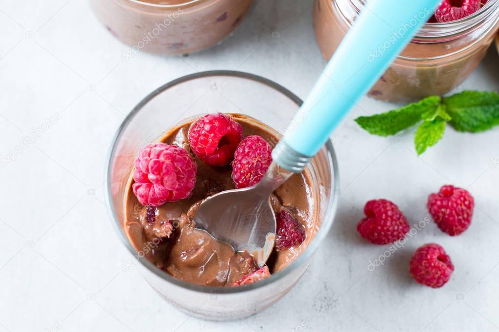 Chocolate mousse with fresh raspberry with a spoon in a glass jar