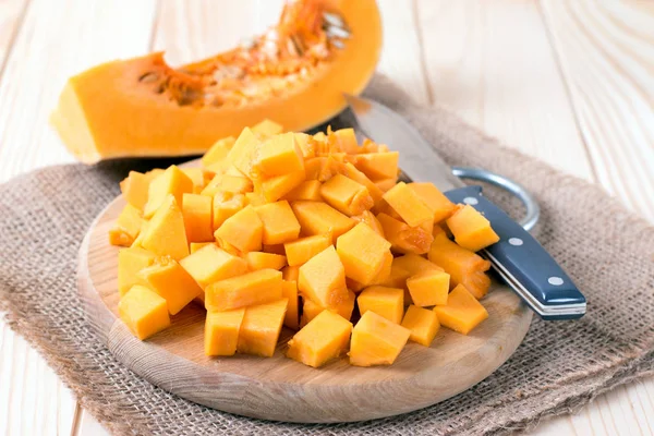 Cubos de calabaza en tabla de cortar y cuchillo en mesa de madera — Foto de Stock