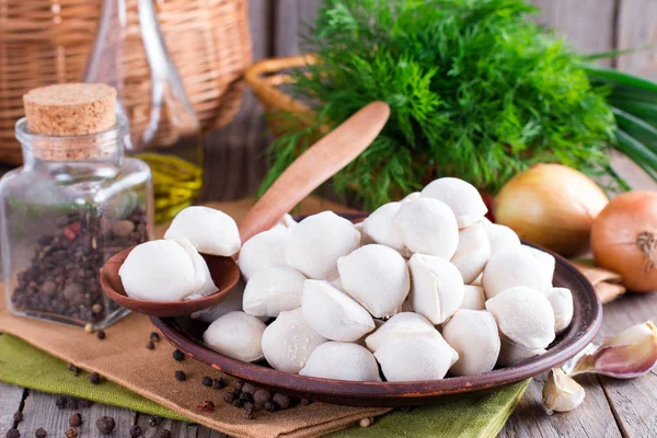 Pequeñas albóndigas congeladas en plato marrón sobre mesa de madera. Raviolis caseros. Albóndigas rusas. Pelmeni. — Foto de Stock