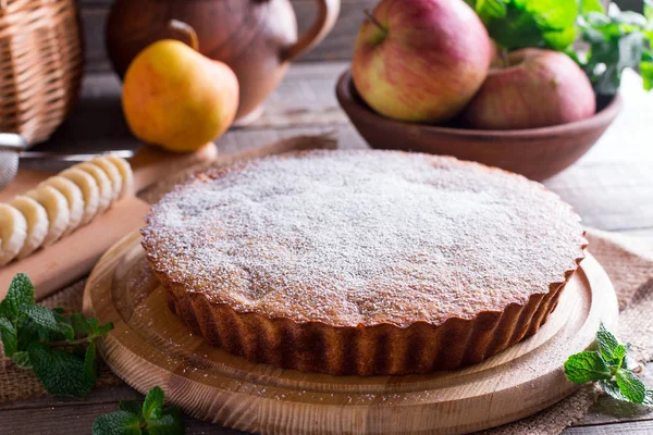 Cake met walnoten en een banaan met poedersuiker op een houten achtergrond — Stockfoto