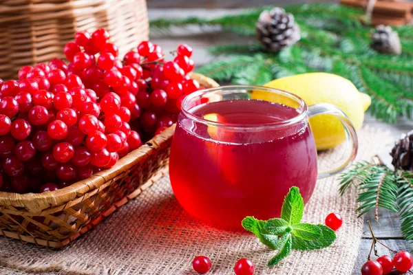 Té de viburnum rojo fresco en un vaso transparente sobre un fondo de madera, cerca de la rama con bayas rojas de viburnum — Foto de Stock