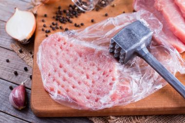 Tenderization of fresh pork steak on wooden chopping board clipart