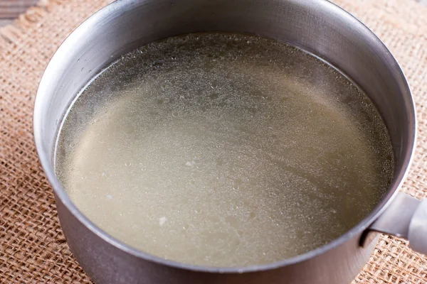 Caldo amarelo dourado em uma panela em uma mesa de madeira — Fotografia de Stock