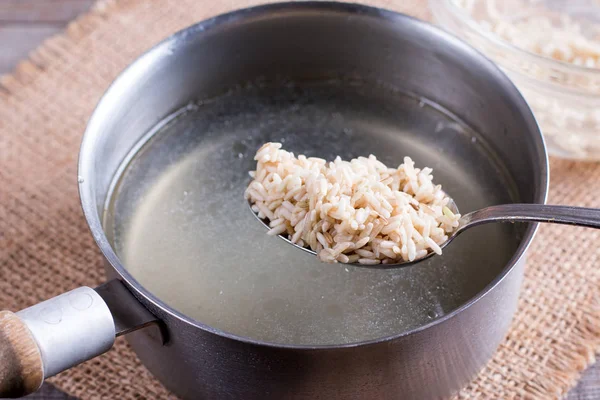 Рис в ложке в кастрюле с кипящим бульоном на деревянном столе — стоковое фото