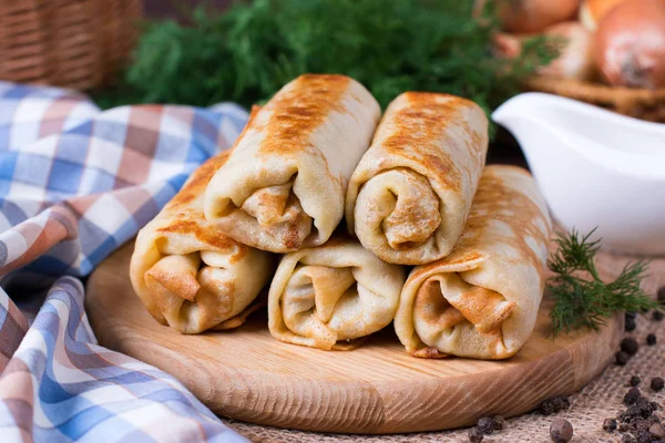 Panqueques finos con rellenos con eneldo en una tabla de cortar sobre una mesa de madera — Foto de Stock