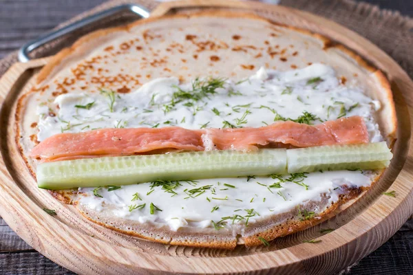 Pancake stuffed with cream cheese, dill, salmon and cucumber on a chopping wooden board — Stock Photo, Image