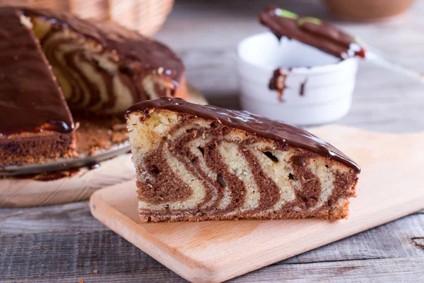 Piece of ''Zebra'' cake with chocolate glaze on wooden table — Stock Photo, Image