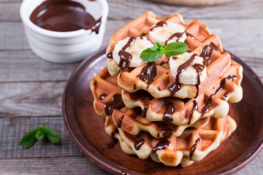 Çikolata şurubu ve muz dilimi ahşap arka plan üzerinde bir tabakta Belçika waffle
