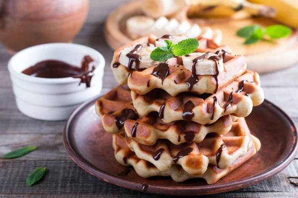 Belgian waffles with chocolate syrup and banana slice on a plate on a wooden background — Stock Photo, Image