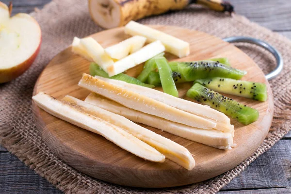 Tranches de fruits sur une planche à découper (kiwi, banane, pomme) sur une table — Photo