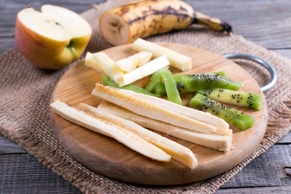 Шматочки фруктів на обробній дошці (ківі, банан, яблуко) на столі — стокове фото