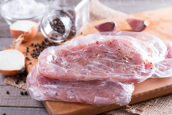 Fresh raw pork chops meat in a bag on chopping board on wooden desk