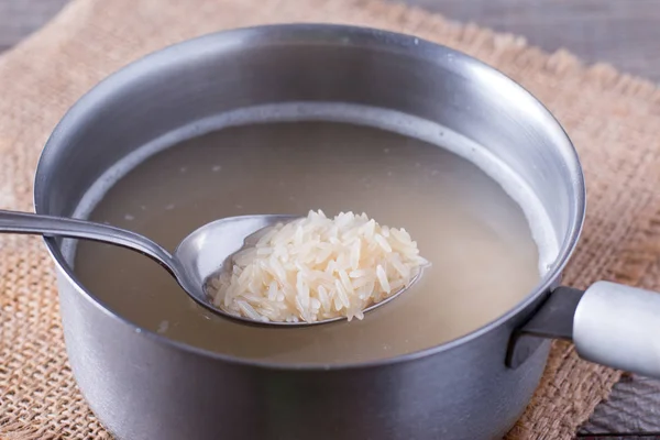 Colher com arroz cru sobre panela em mesa de madeira — Fotografia de Stock