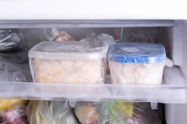 A container with food in the freezer. A freezer packed with chicken, soup and various frozen food clipart
