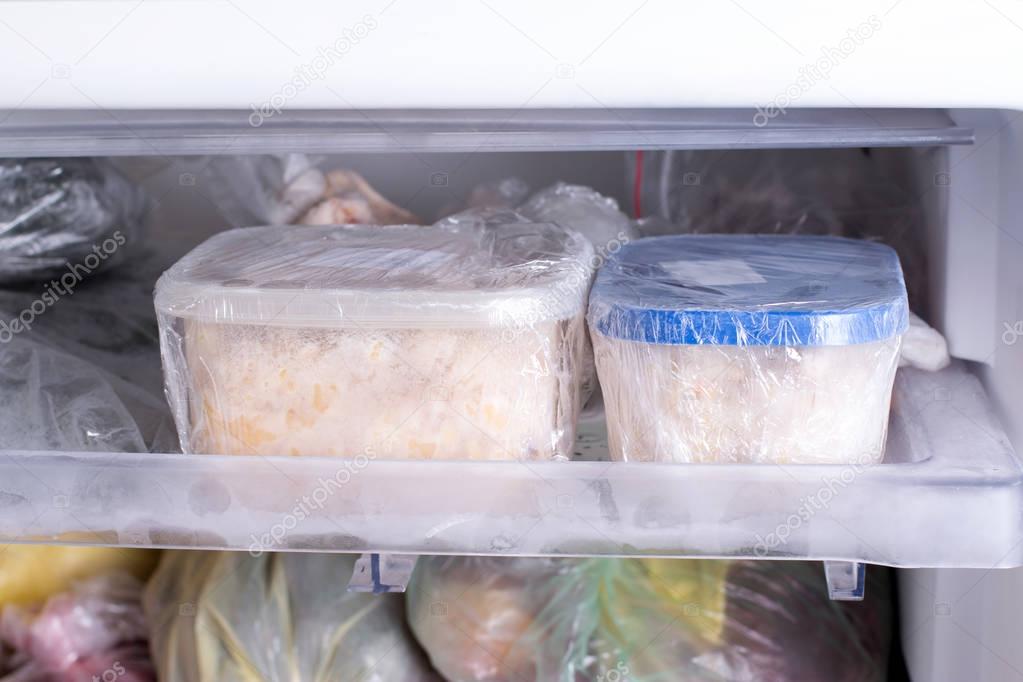A container with food in the freezer. A freezer packed with chicken, soup and various frozen food