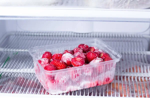 Fresas congeladas en un recipiente de plástico en el congelador — Foto de Stock