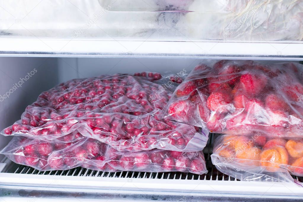 Frozen berries and fruits in bags in freezer, close up