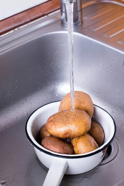Картошка моется под проточной водой. Картофель моют под водопроводной водой . — стоковое фото