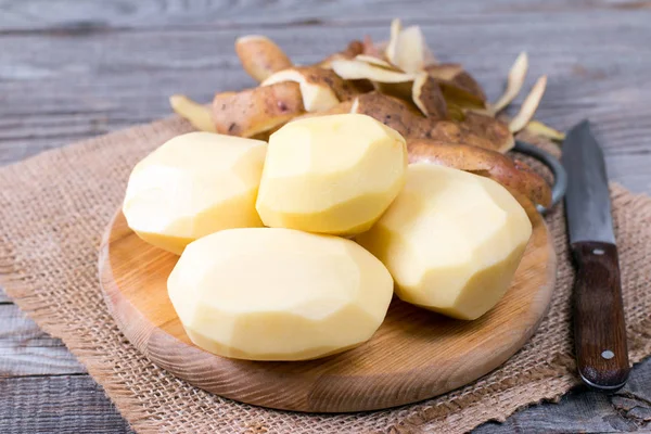 Geschälte Kartoffeln mit Schale und Messer auf einem Holztisch — Stockfoto