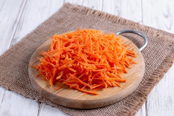 Тертая морковь на разделочной доске на столе — стоковое фото