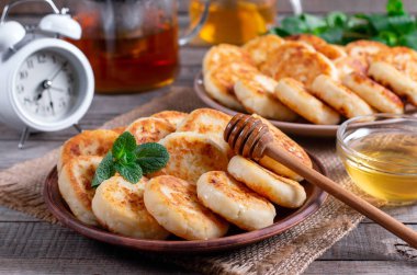 Cottage cheese pancakes, syrniki with honey on a plate on wooden background