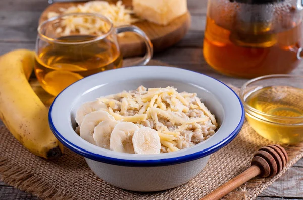 Oatmeal porridge with cheese and banana on a white plate on a wooden background — Stockfoto