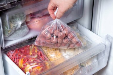 Buzdolabına köfteli plastik poşet ve donmuş sebze koyan adam, yakın plan.
