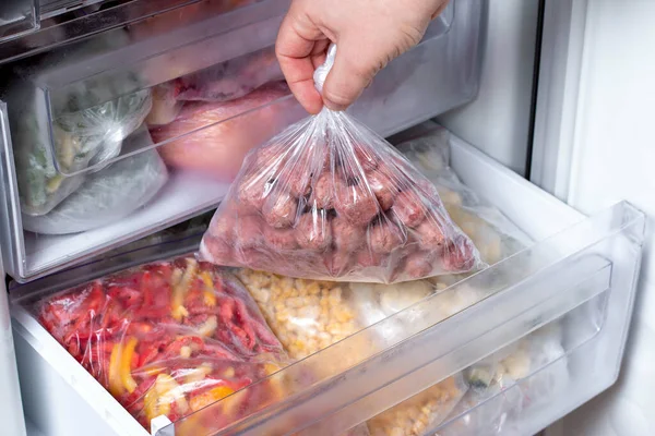 男人把装有肉丸子的塑料袋放进冰箱 里面装着冷冻蔬菜 特写镜头 — 图库照片
