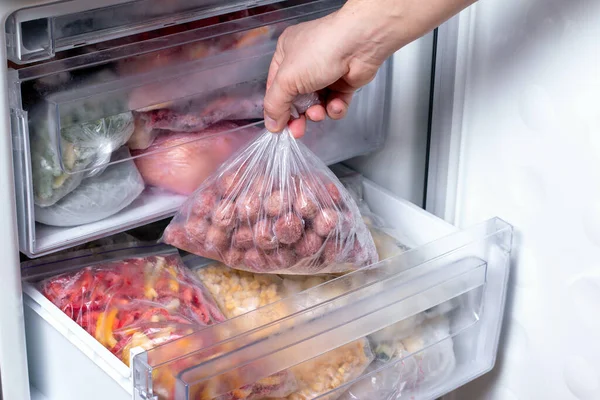 男人把装有肉丸子的塑料袋放进冰箱 里面装着冷冻蔬菜 特写镜头 — 图库照片