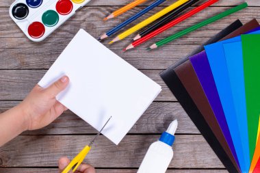 Çocuk bir kağıt şerit kare tutuyor ve onu kesiyor. Çocuk el işi yapıyor. Tahta masaya yapıştırıcı, kağıt, makas. Çocuk sanat projesi, çocuklar için bir zanaat..