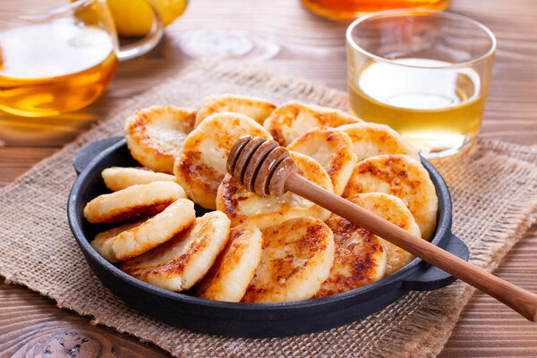 Оладьи из творога с медом на тарелке на деревянном фоне. Завтрак
