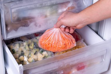 Buzdolabına havuç ve donmuş sebze dolu plastik poşet koyan adam, yakın plan.