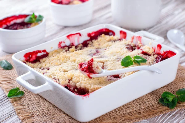 Berry crumble in white dish on white wooden background