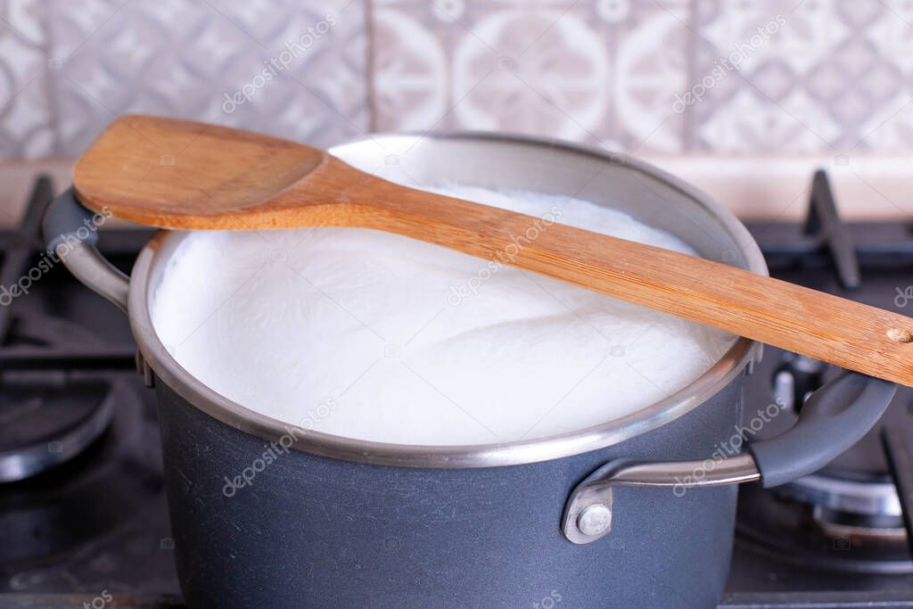 Boiling milk in a pan, wood spoon on the top, closeup