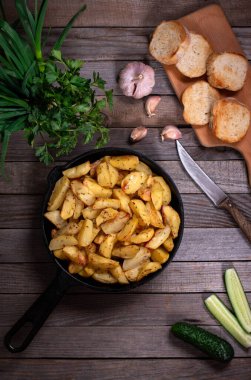 Kırsal tarzda kızarmış patates, baharatlar ve taze yeşilliklerle, ahşap bir masanın üzerinde. Kızarmış patates. Üst görünüm.